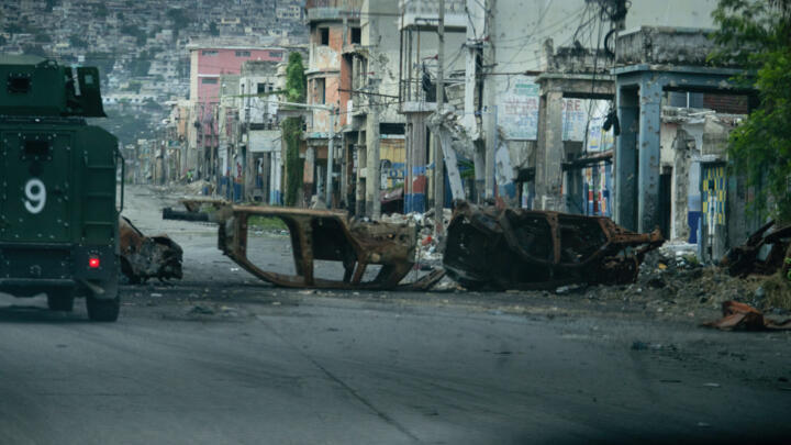 In this file photo, a police vehicle drives around cars burned by armed gangs and used as a barricade during clashes last week with Haitian security forces on a deserted street in the city center, seen from an armored police vehicle during a patrol, in Port-au-Prince on January 16, 2026.