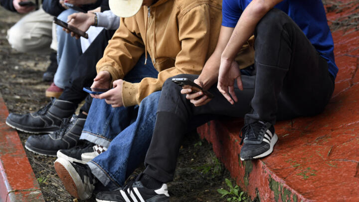 Teenagers use their smartphones at the entrance of their high school in Seville, Spain on February 6, 2026