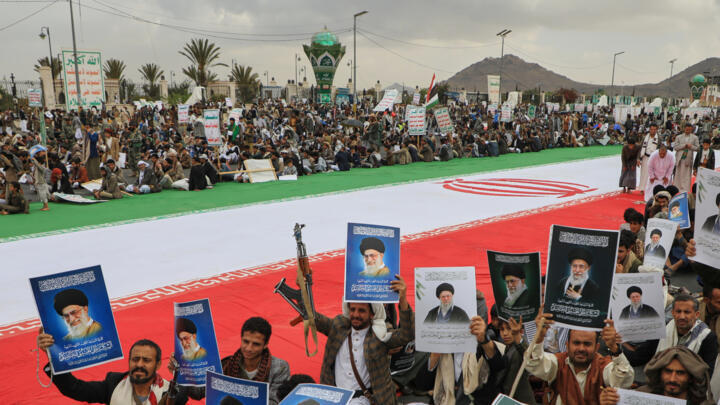 Houthi supporters hold posters of Iran's late Supreme Leader Ayatollah Ali Khamenei, who was killed in an attack by Israel and the U.S., next to a giant Iranian flag as they protest the war on Iran.