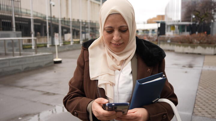 Syrian human rights defender Yasmen Almashan looks at a photo of her brothers, who were killed during the Assad regime, on her phone in front of the UN in New York on March 12, 2026.